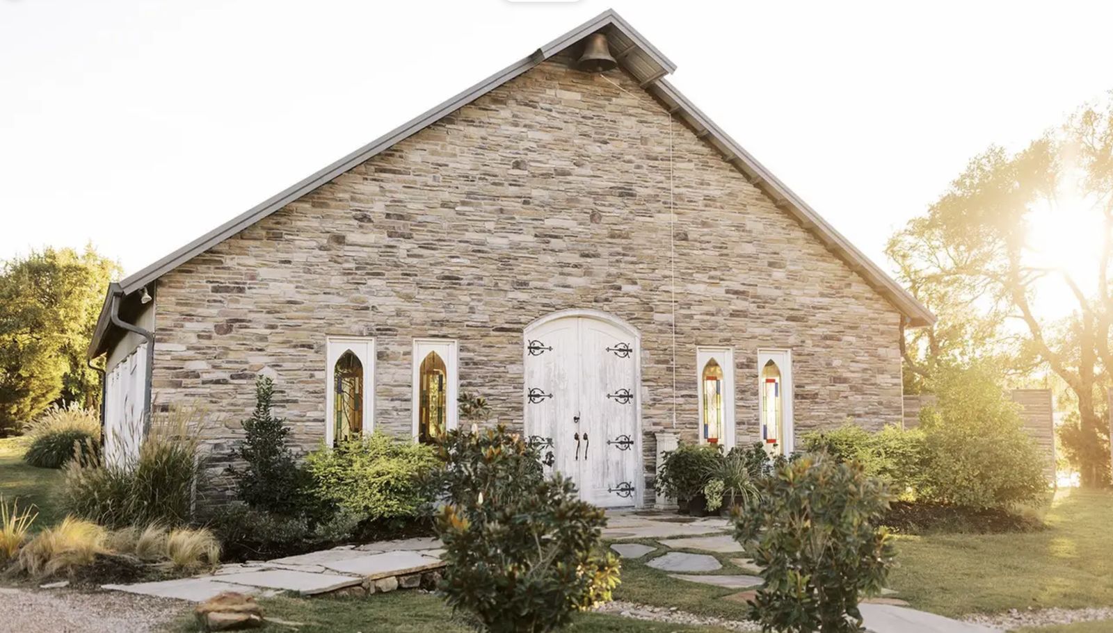 A stone chapel with white arched doors and stained glass windows
