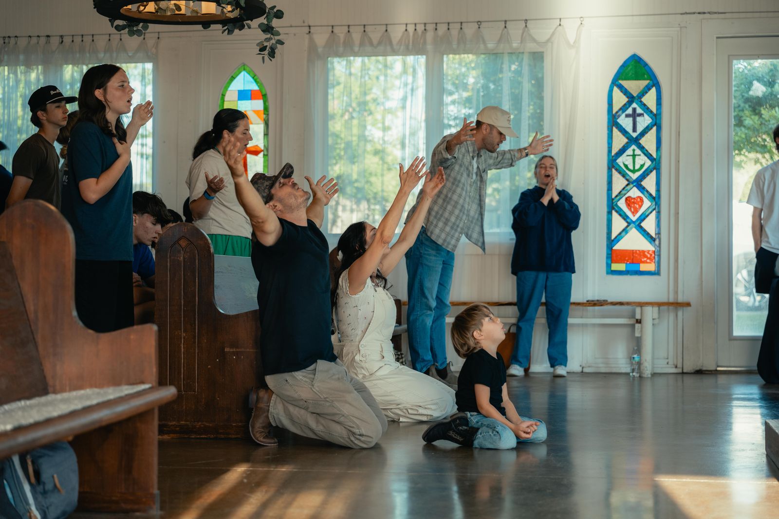 Theo and Rachel Koulianos kneeling with hands raised in worship in a chapel, their young son sitting beside them