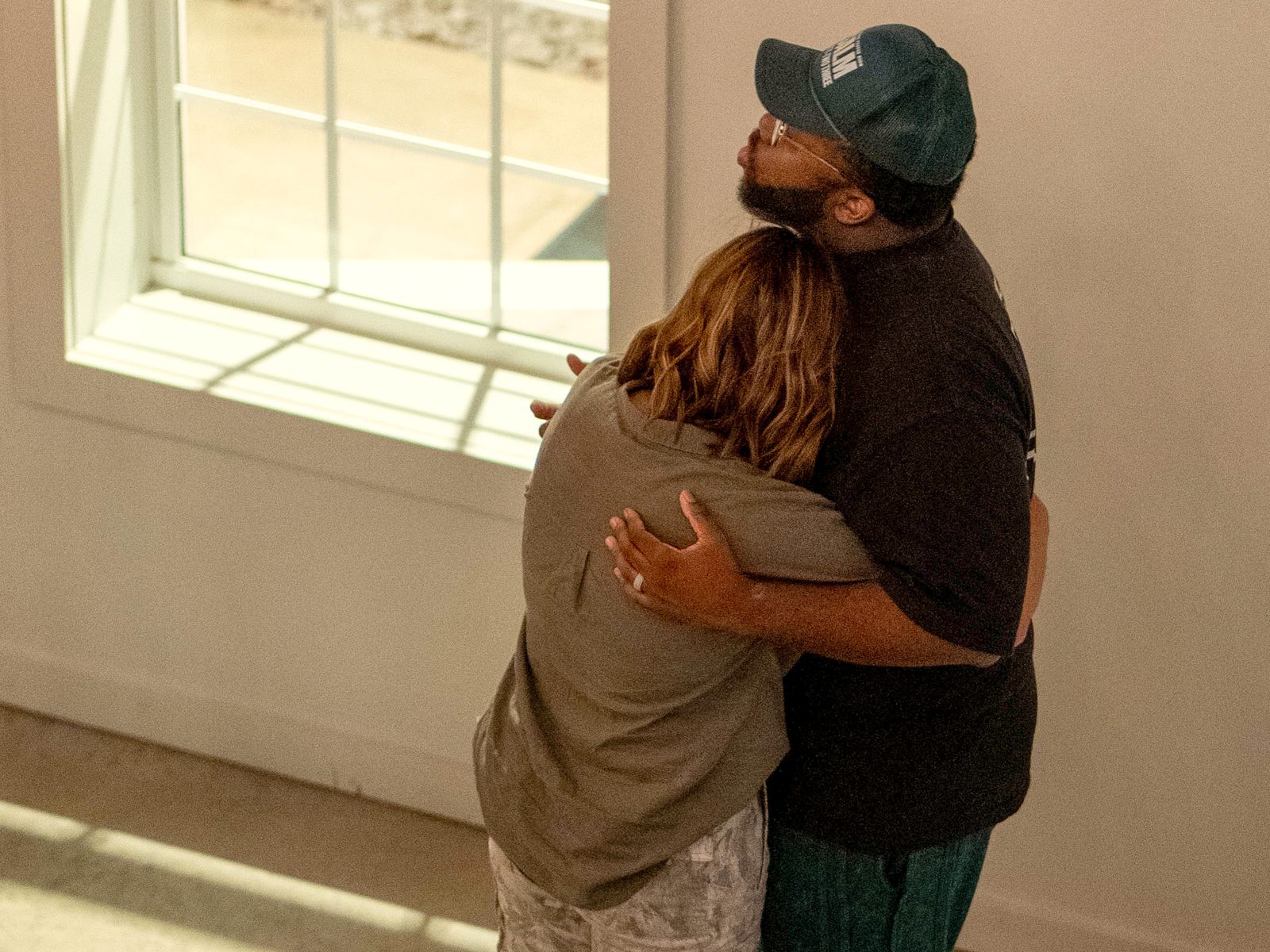 A husband and wife holding each other in a long embrace by a sunlit window