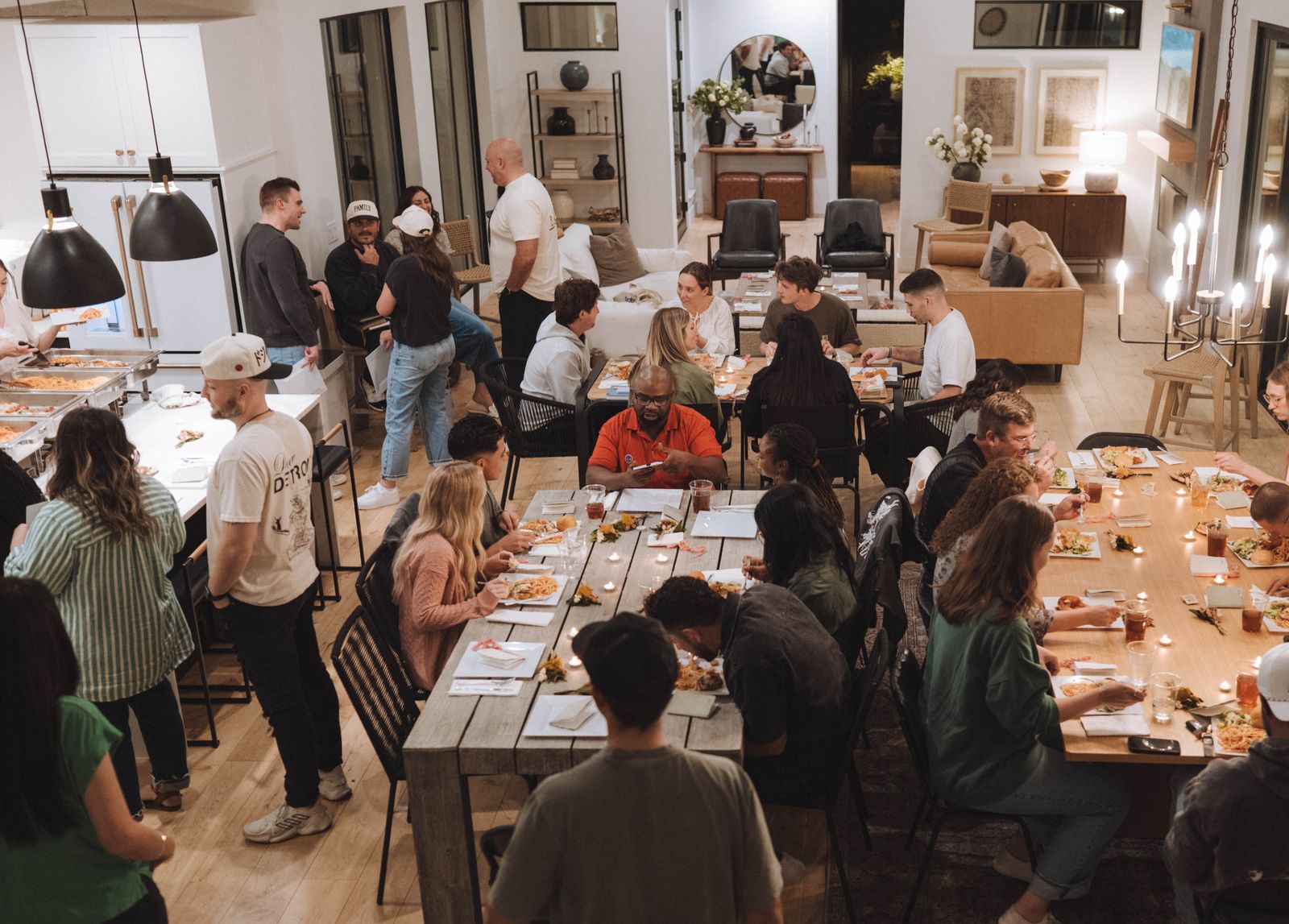 A diverse group of young couples sharing dinner around long tables in an open home during a private intensive