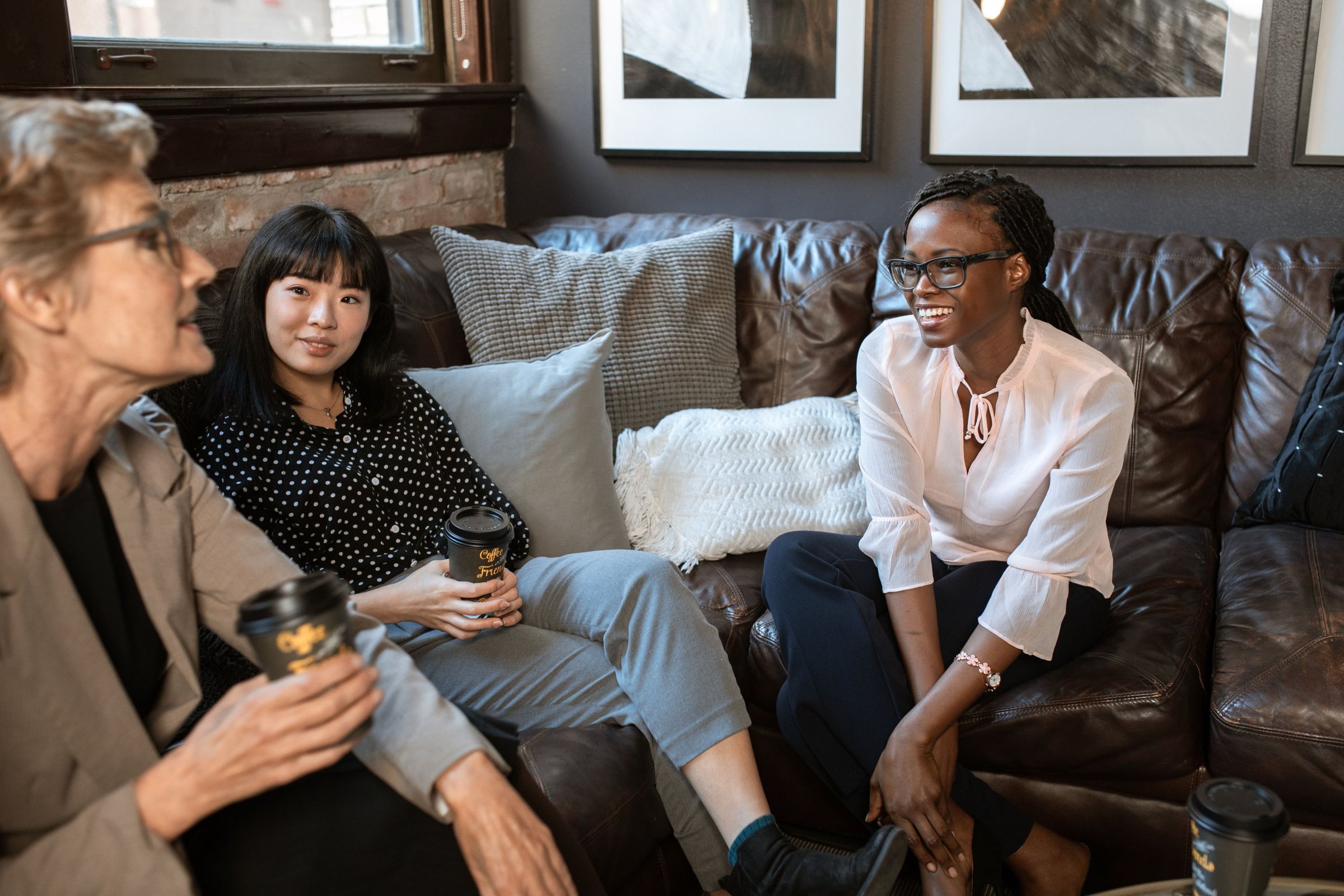 Women gathered on a cozy living room couch, sharing coffee and laughing together